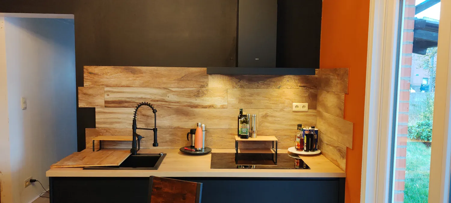Cuisine aménagée avec mobilier sombre, évier et crédence à aspect bois